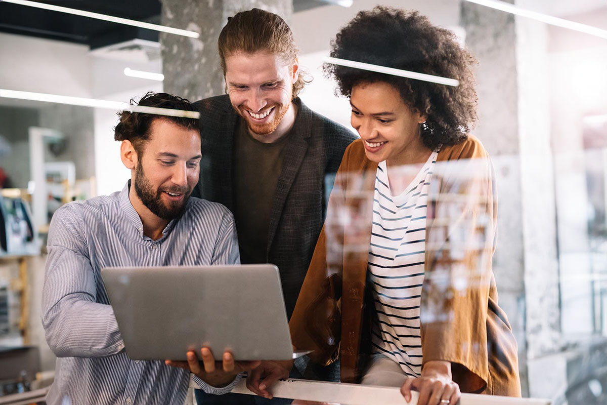 A group of 3 workers gathered around a laptop smiling