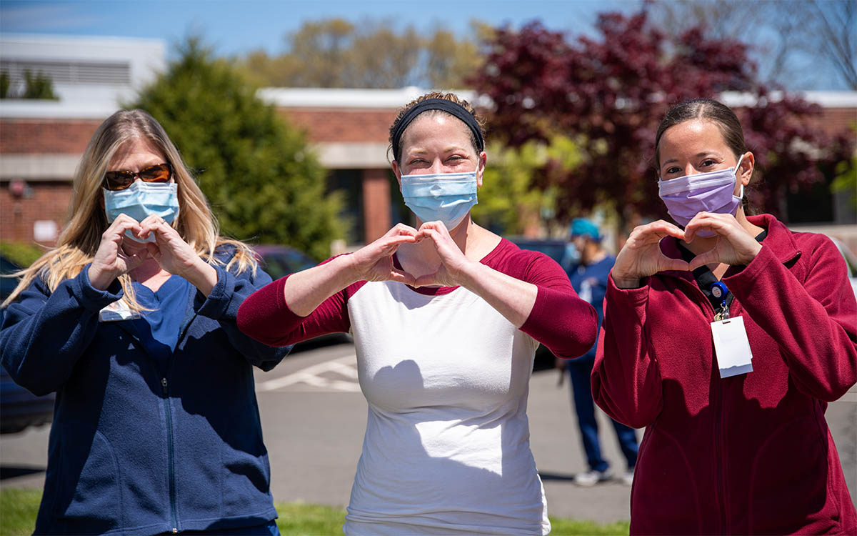 Three workers wearing face masks making hearts with their hands