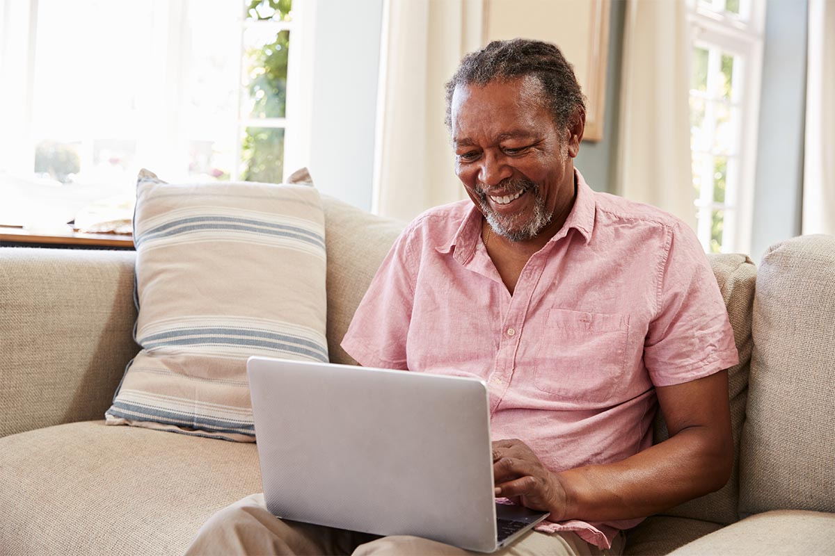 Senior Man Sitting On Sofa Using Laptop At Home