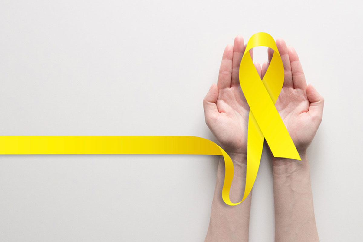 A pair of hands are held outstretched holding a yellow ribbon representing suicide prevention.