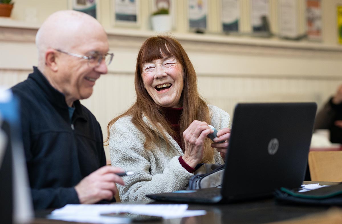 Two elderly colleagues laughing around a laptop