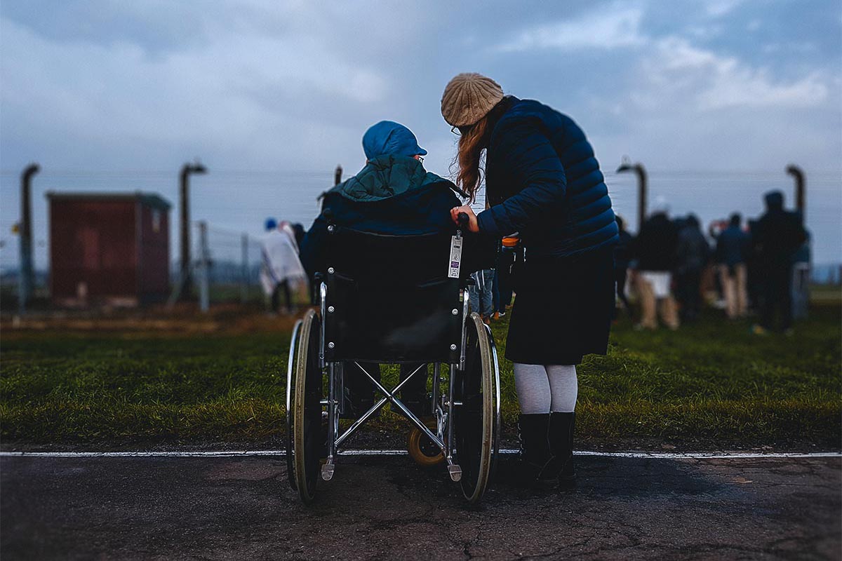 Person in a wheelchair next to their carer, looking off into the distance.